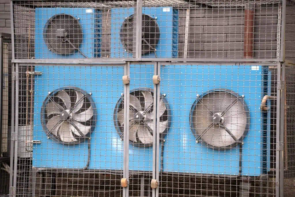 Industrial HVAC ventilation fans behind protective metal grid.