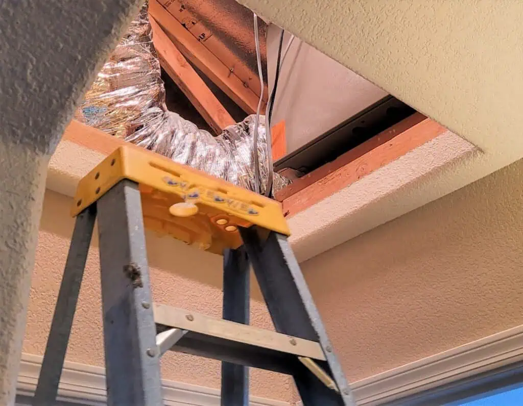HVAC ductwork being installed through ceiling opening in attic space.